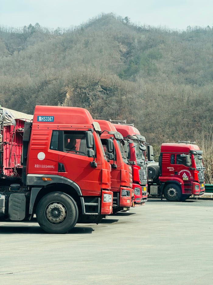 Array of red cargo trucks parked outdoors in a mountainous area during day.